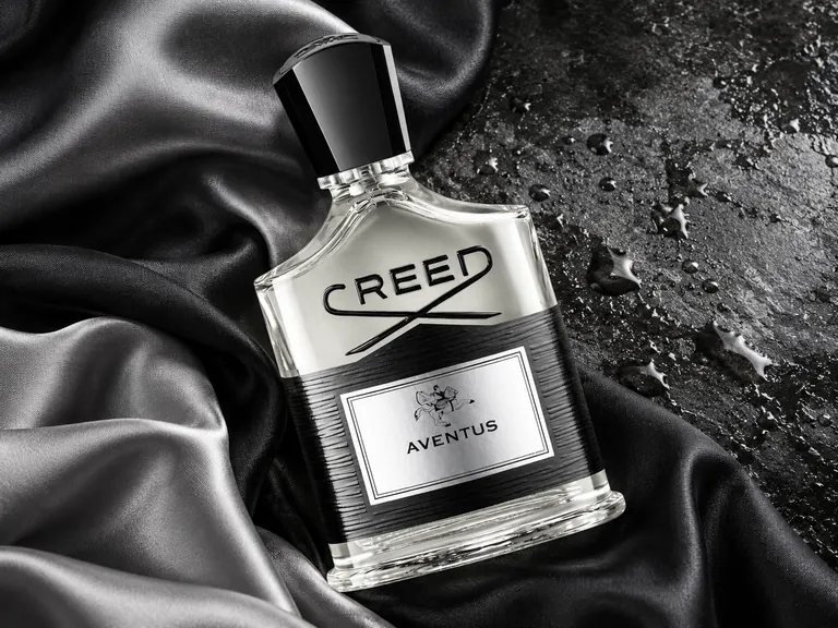 Editorial illustration: a men's fragrance bottle with a black cap resting on black satin beside a dark, water-beaded surface